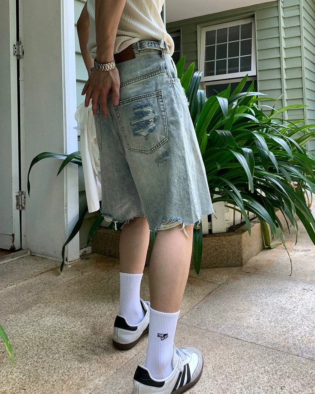 Light blue distressed raw-hem denim shorts, side showing back-pocket distressing